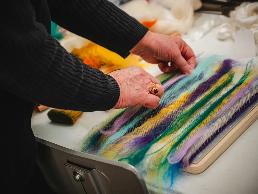 Manos extendiendo mechas de lana de colores sobre una mesa de taller durante el proceso de afieltrado
